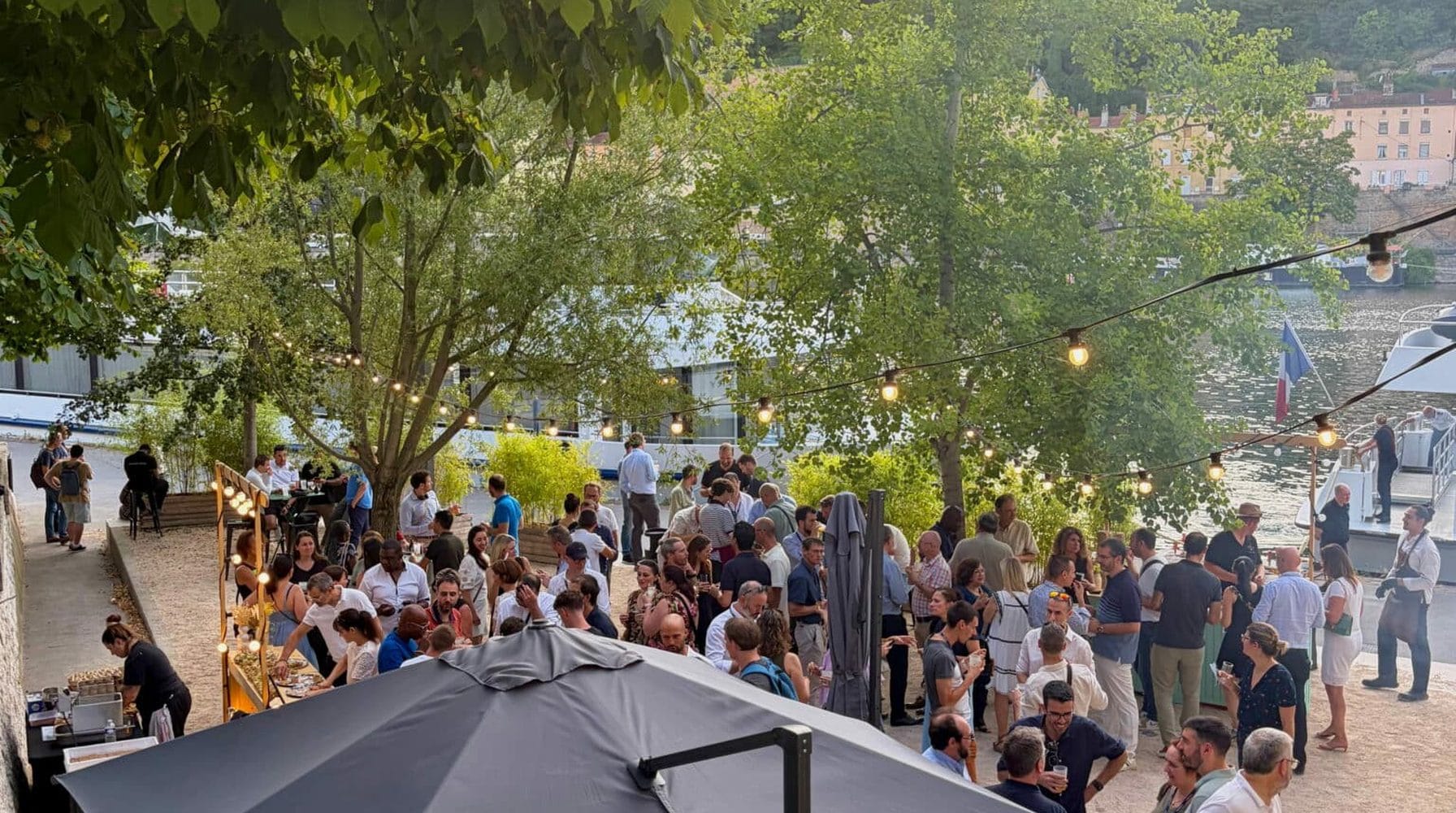 Food court événementiel sous les arbres : convives et stands de restauration en extérieur.