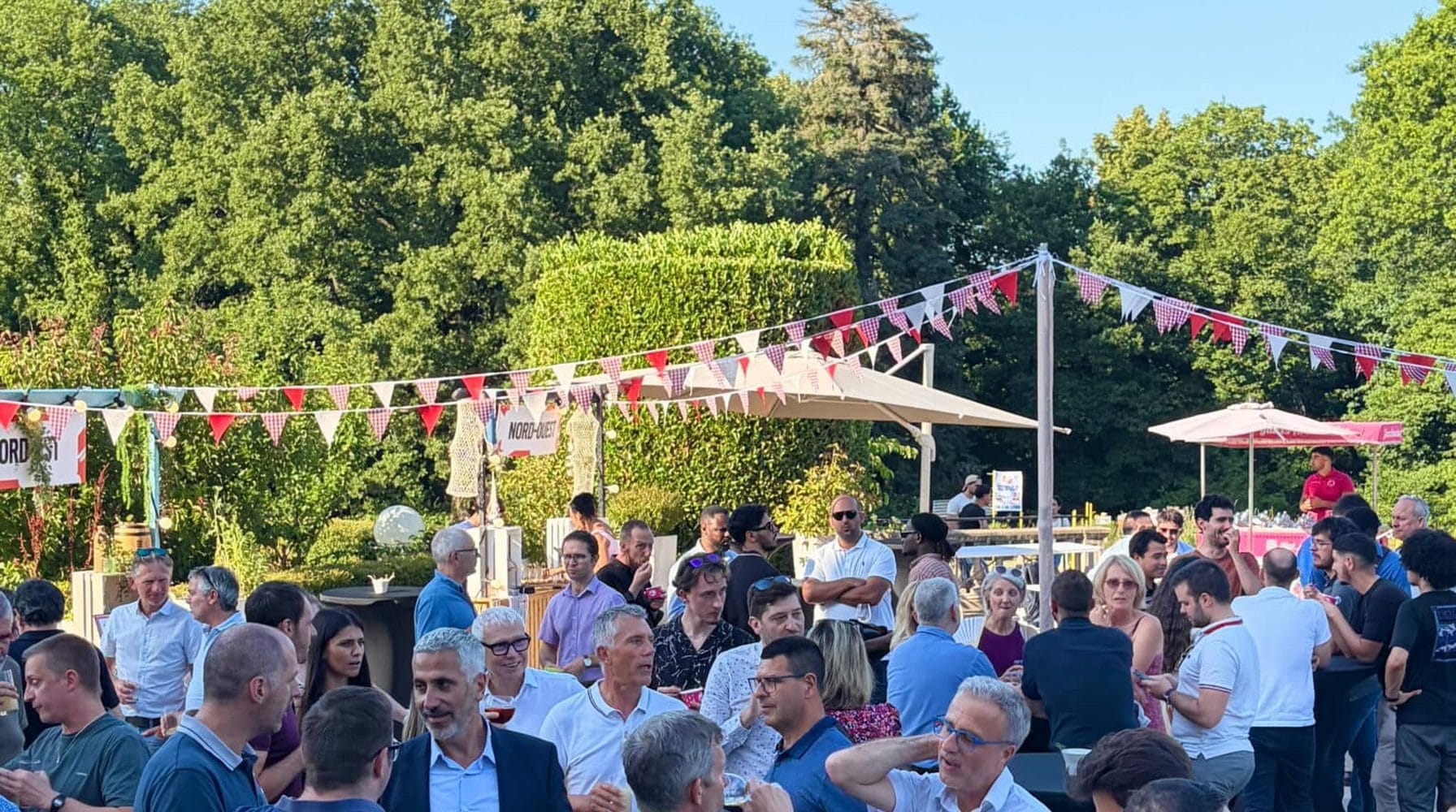 Cocktail d'entreprise en extérieur, guirlandes de fanions et convives réunis en terrasse.