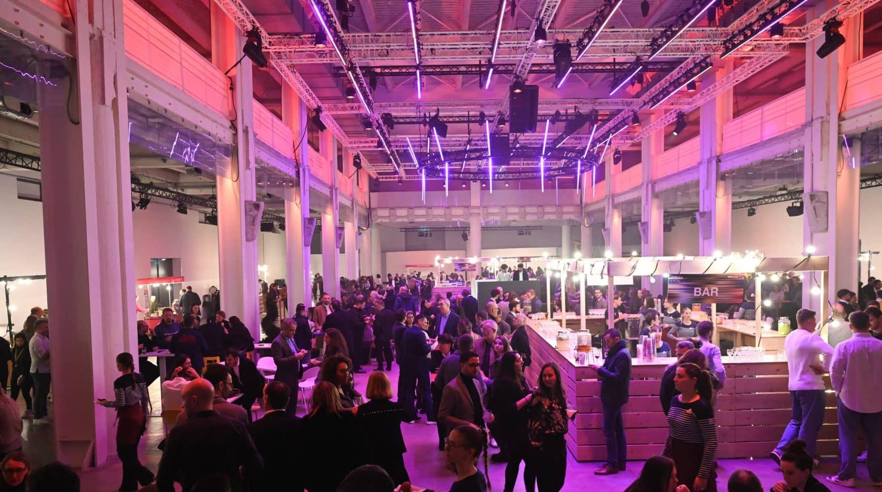 Soirée de gala d'entreprise dans une grande halle éclairée, avec bar et convives.